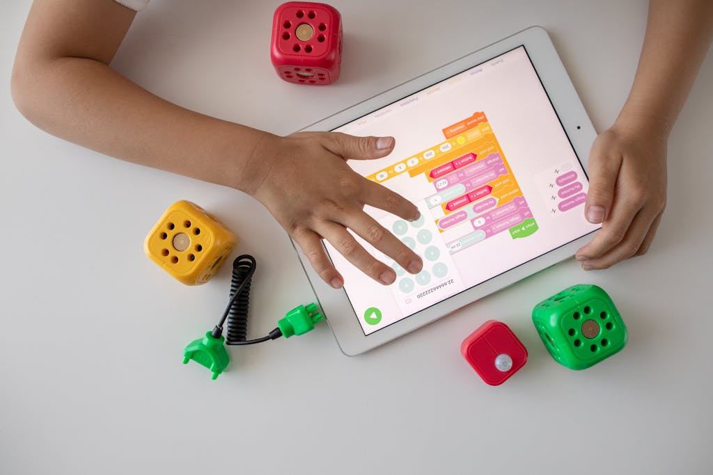 Child using digital tablet for coding education alongside colorful toy blocks.