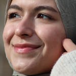Close-up portrait of a smiling woman wearing a hijab outdoors, radiating joy.