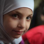 Dreamy girl with big grey green eyes in white hijab looking at camera with half smile on blurred background